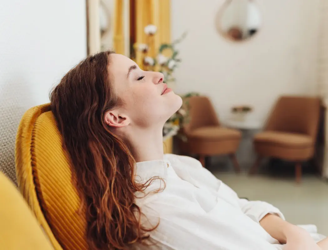 Woman relaxing in a yellow armchair with her eyes closed.